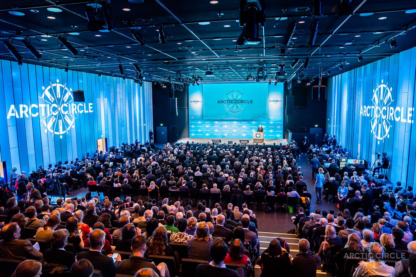 Big conference room filled with people. Arctic Circle Assembly logo is visible on big screens.